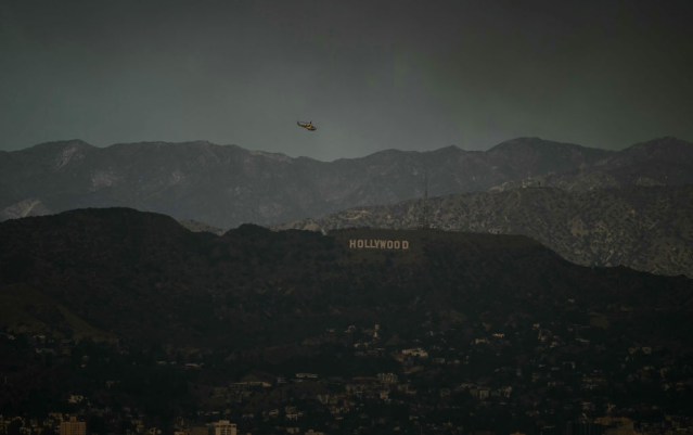 A firefighting helicopter flies above the hollywood sign as the sky is engulfed in dark smoke from the many fires burning around the city, as seen from Kenneth Hahn State Recreation Area in Los Angeles, on January 8, 2025. Rampaging wildfires around Los Angeles have killed at least two people, officials said January 8 as terrifying blazes leveled whole streets, torching cars and houses in minutes.More than 1,000 buildings have burned in multiple wildfires that have erupted around America's second biggest city, forcing tens of thousands of people from their homes. (Photo by Patrick T. Fallon / AFP) (Photo by PATRICK T. FALLON/AFP via Getty Images)