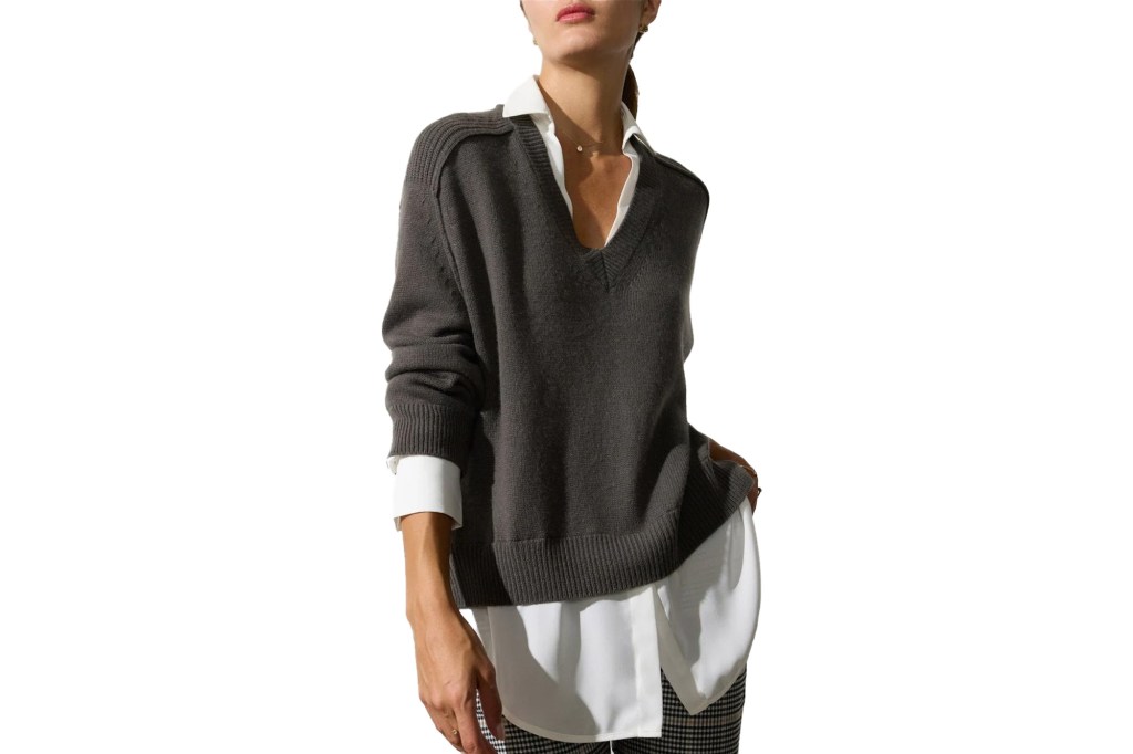 A woman in a dark gray V-neck sweater over a white collared shirt and plaid pants.