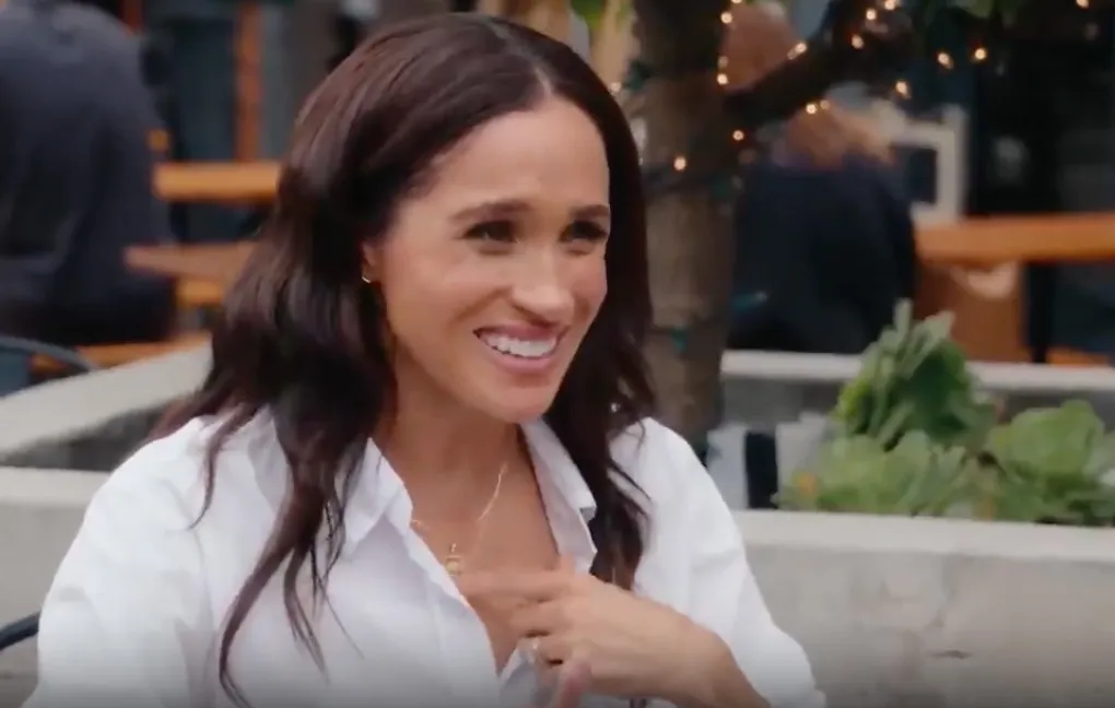 Meghan Markle laughing and touching her chest.