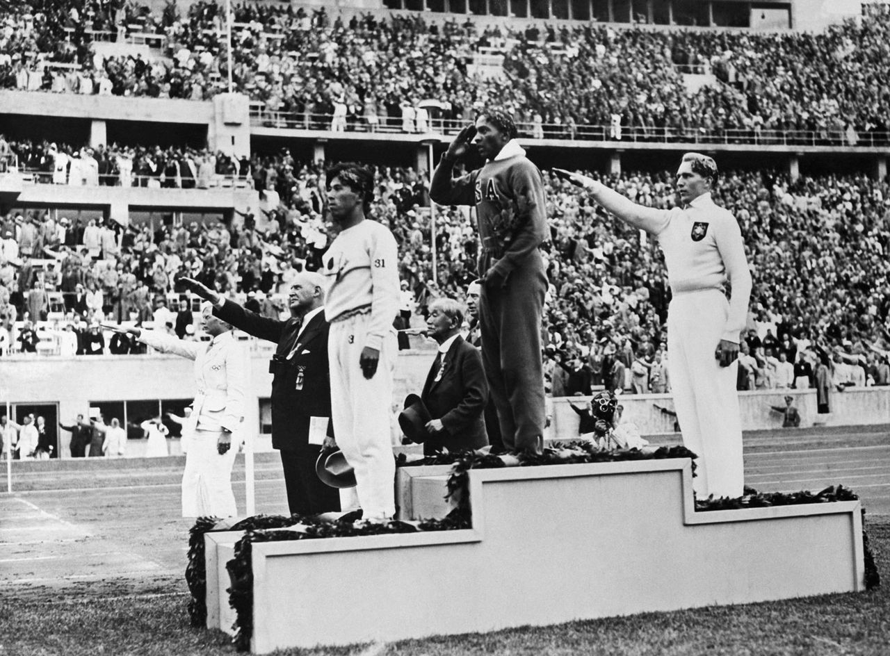 The gold, silver and bronze medal winners in the long jump competition salute from the victory stand at the 1936 Summer Olympics in Berlin. From left, Japan's Naoto Tajima (bronze), American Jesse Owens (gold) who set an Olympic record in the event and offers an American-style salute with his hand to his forehead, and Germany's Luz Long (silver) giving a Nazi salute with his arm extended out. August 8, 1936. Jesse Owens (center) stands on the podium after winning gold at the 1936 Berlin Olympics Getty