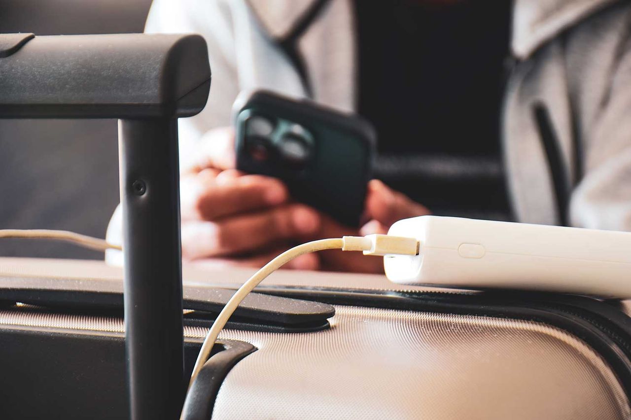 Cropped image of a South Asian man waiting in airport lounge charging his phone using power bank before departure. Focus on the foreground. Getty