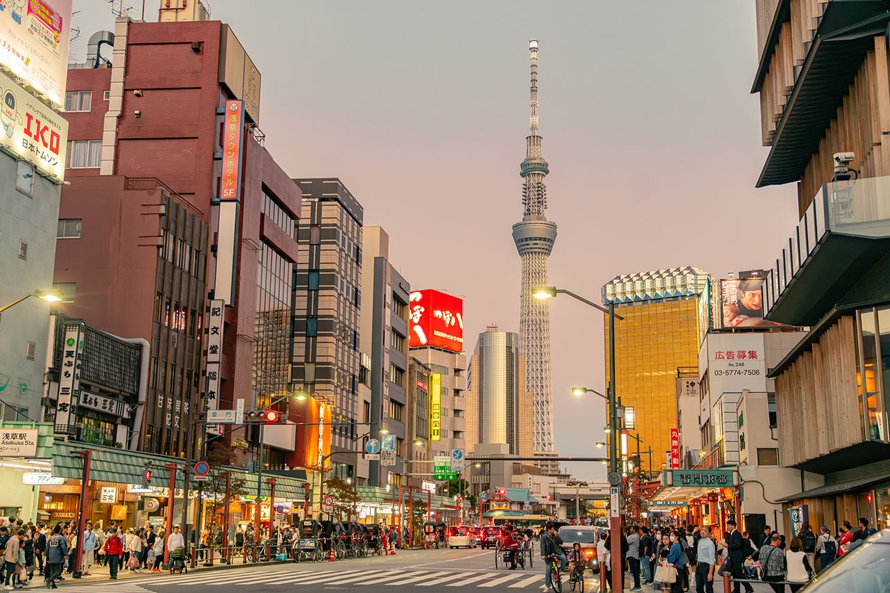 An evening view of the tourist hub of Asakusa, a more traditional part of Tokyo. Shops, restaurants, street lamps, signages and street stalls are visible in the image. A large number of people are waiting to cross the road. The Tokyo Skytree or Sky Tree is visible in the background. The Tokyo Skytree tower in the center of Tokyo, Japan's capital Getty