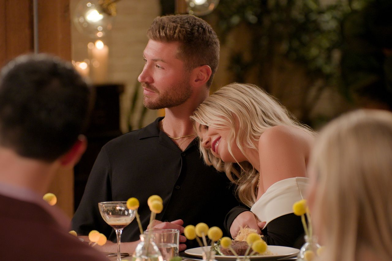 Two people seated at a dinner table with the woman leaning her head on the mans shoulder Andrew and Libby in 'Age of Attraction'Credit: Netflix