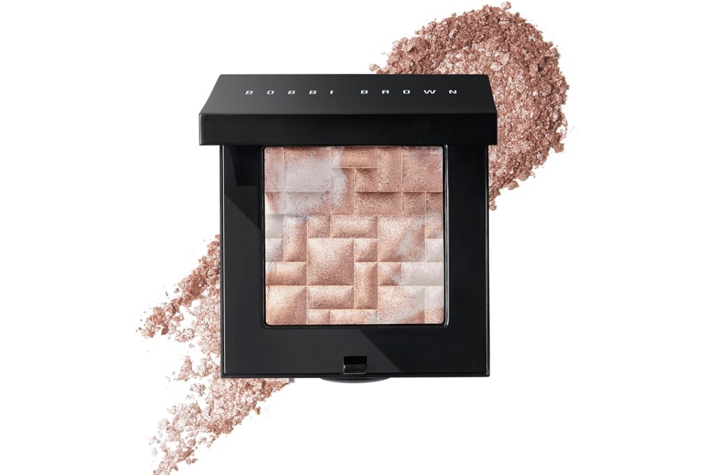 Bobbi Brown Shimmer Brick compact in a black case with an open lid, showing a mosaic pattern of light and dark rose gold shimmer powder, with loose shimmer powder scattered around.