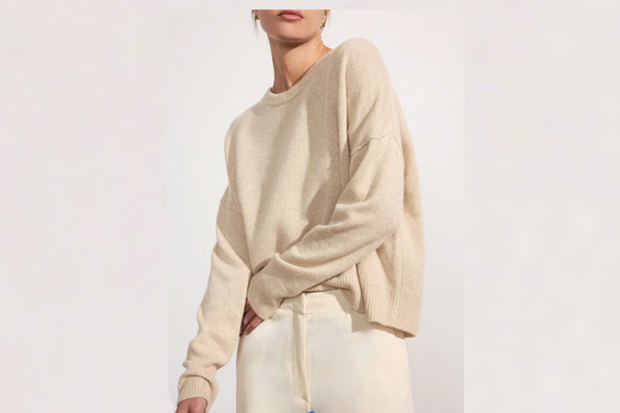 A woman wearing a beige cashmere sweater and light-colored pants.