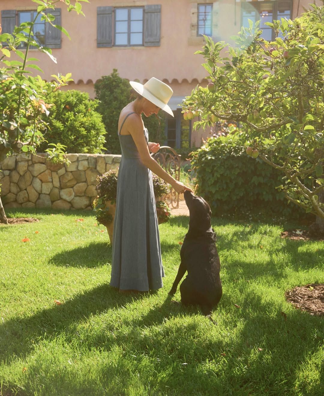 Meghan Markle petting a black dog in a garden.