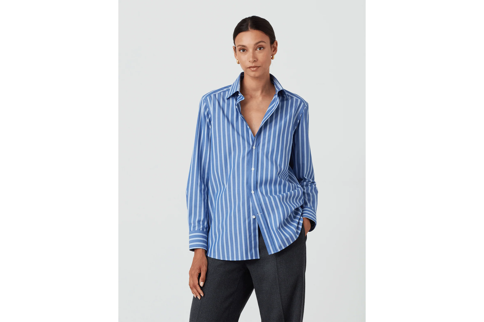 A woman wearing a blue and white striped button-down shirt and charcoal pants.