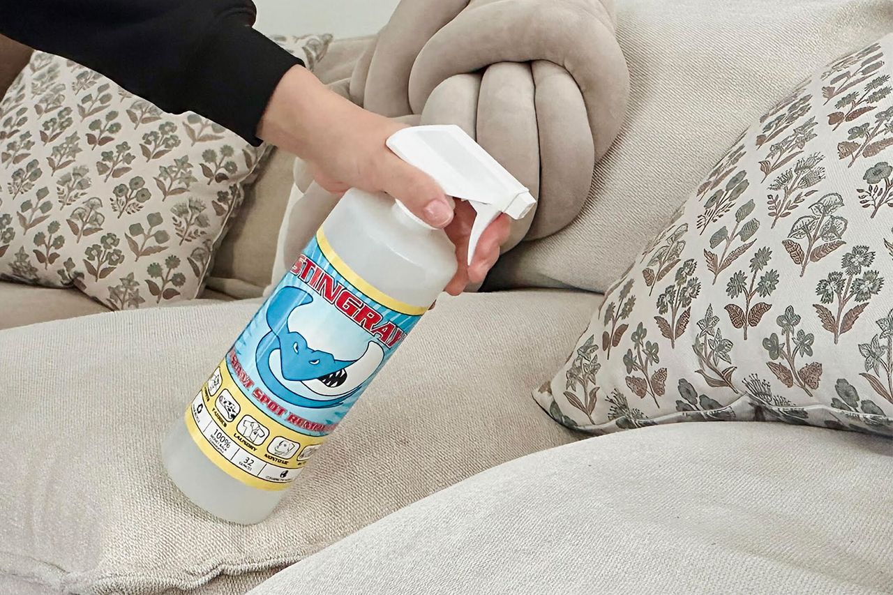 A hand holding a cleaning spray bottle labeled Stingray near a couch Credit: People