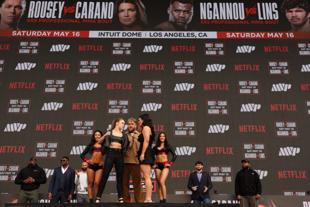 Ronda Rousey (L) and Gina Carano (R) face off in front of Jake Paul (C) during the Most Valuable Promotions (MVP) and Netflix 5X5 Professional MMA bound pre-fight press conference outside the Intuit Dome in Inglewood, California on March 10, 2026. Rousey will face Carano on May 16, 2026. Both fighters will be returning after lengthy retirements. (Photo by Patrick T. Fallon / AFP via Getty Images)