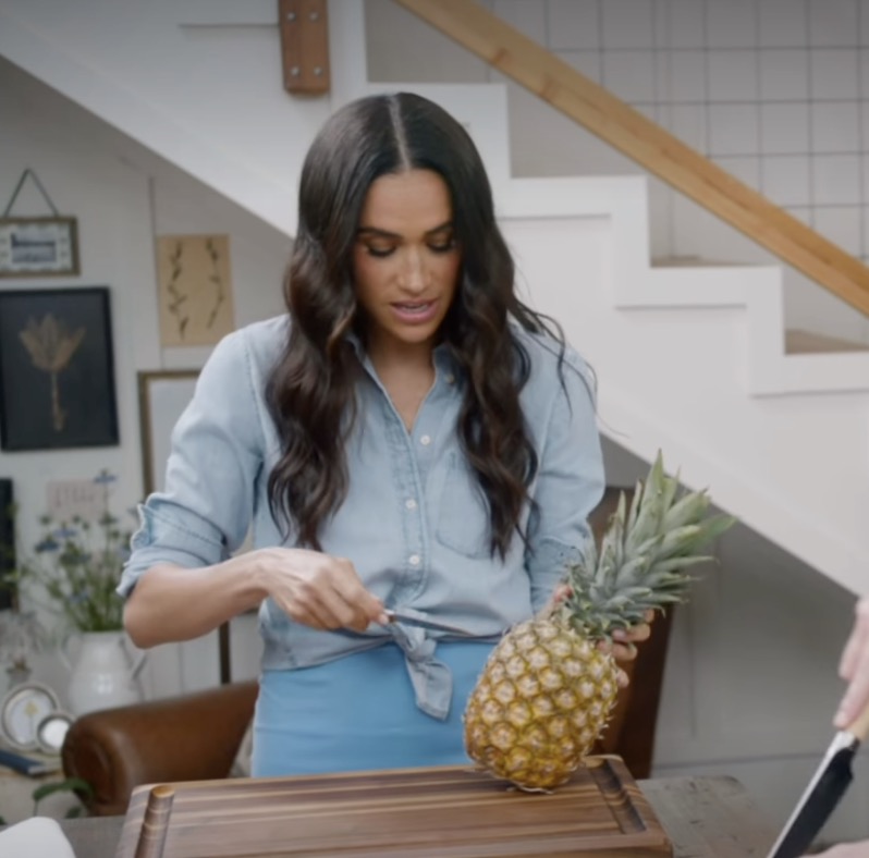 Woman in blue shirt cutting a pineapple.