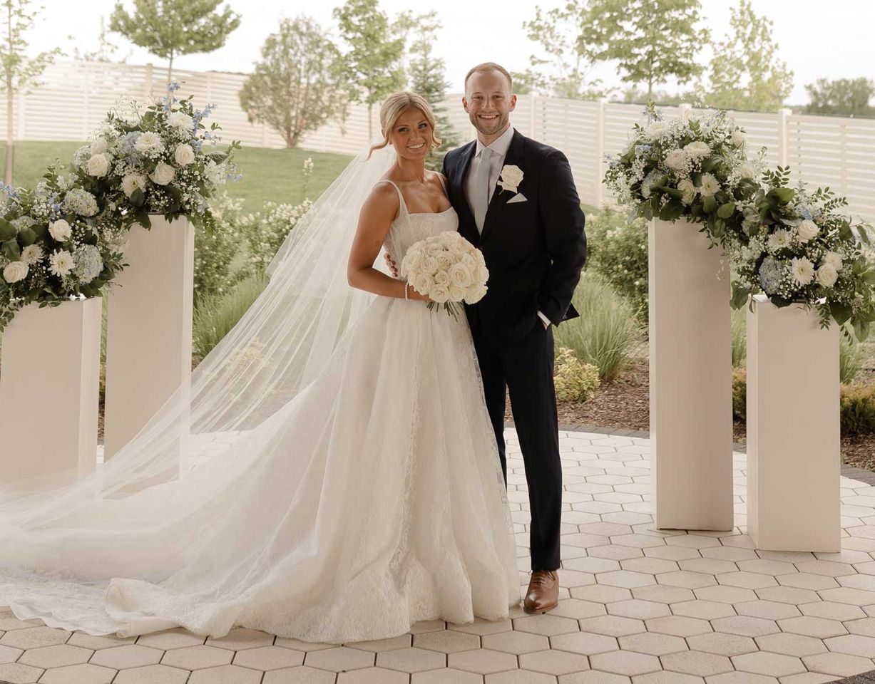 A couple in wedding attire posing outdoors with floral arrangements Kennedy Hannan and Nolan Ruff on their wedding dayCredit: Ivory+Bliss