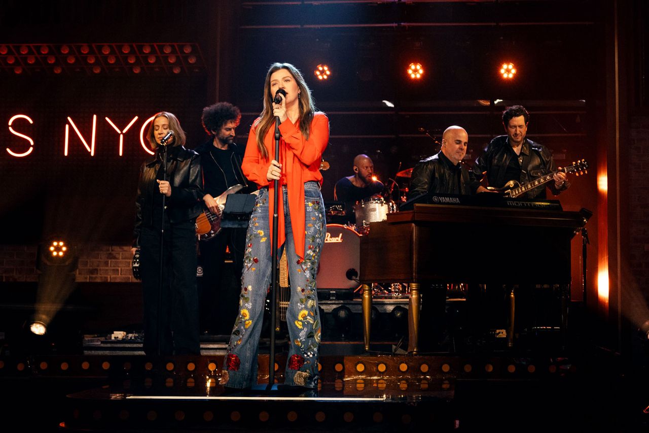 A performer singing on a stage with a live band playing in the background Credit: Weiss Eubanks/NBCUniversal via Getty Images