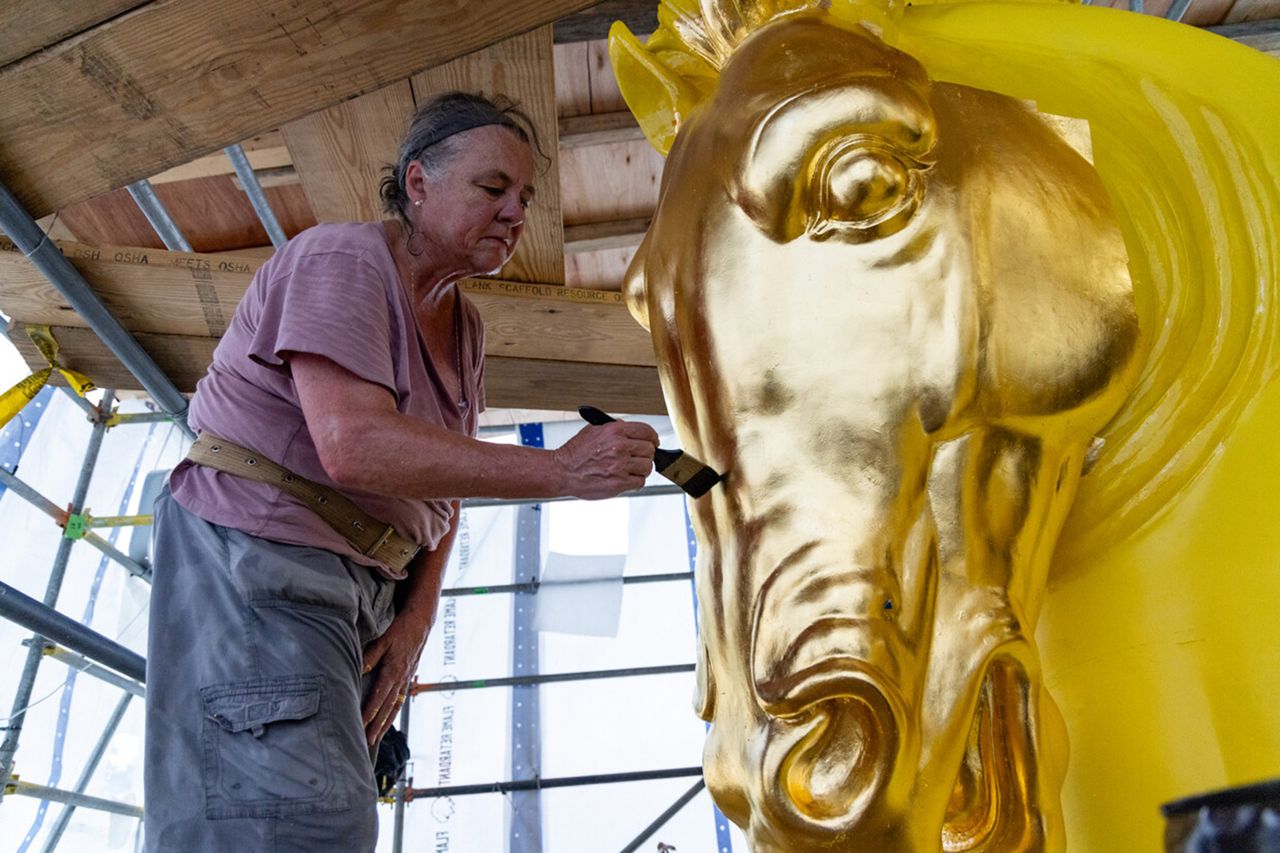 An individual painting a large gold horse sculpture focusing on the headCredit: truth social