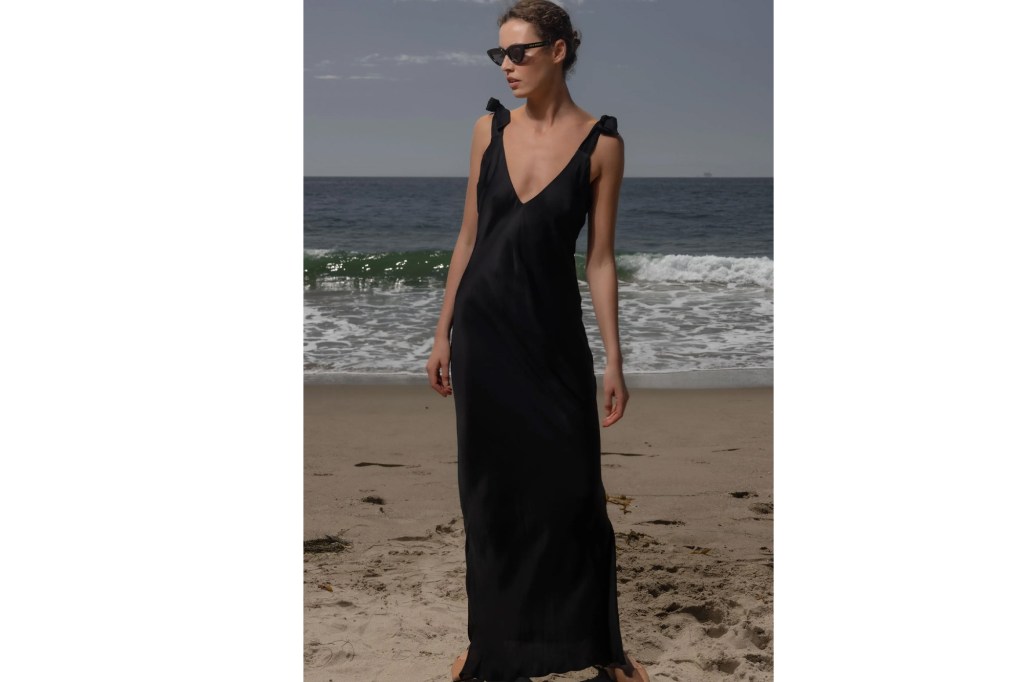 Woman in black maxi dress and sunglasses on a beach.