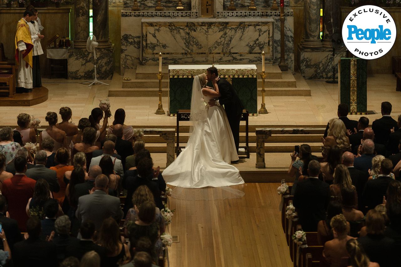 A wedding ceremony in a church the couple kissing at the altar attended by seated guests and officiated by a priest Brandon Bussi and Mary Raclawski’s first kiss as husband and wifeCredit: Nikki Baker Photography