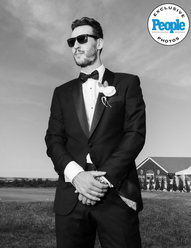A person in formal wear with a boutonniere standing outdoors wearing sunglasses with a house in the background Exclusive Photos watermark present Brandon Bussi’s wedding lookCredit: Nikki Baker Photography