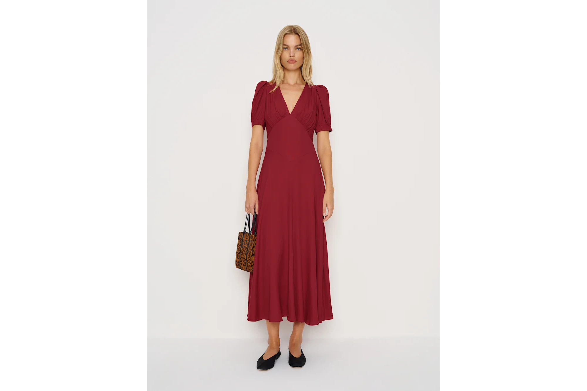 A woman in a red maxi dress with a V-neck, short puffy sleeves, black flats, and a leopard print handbag.