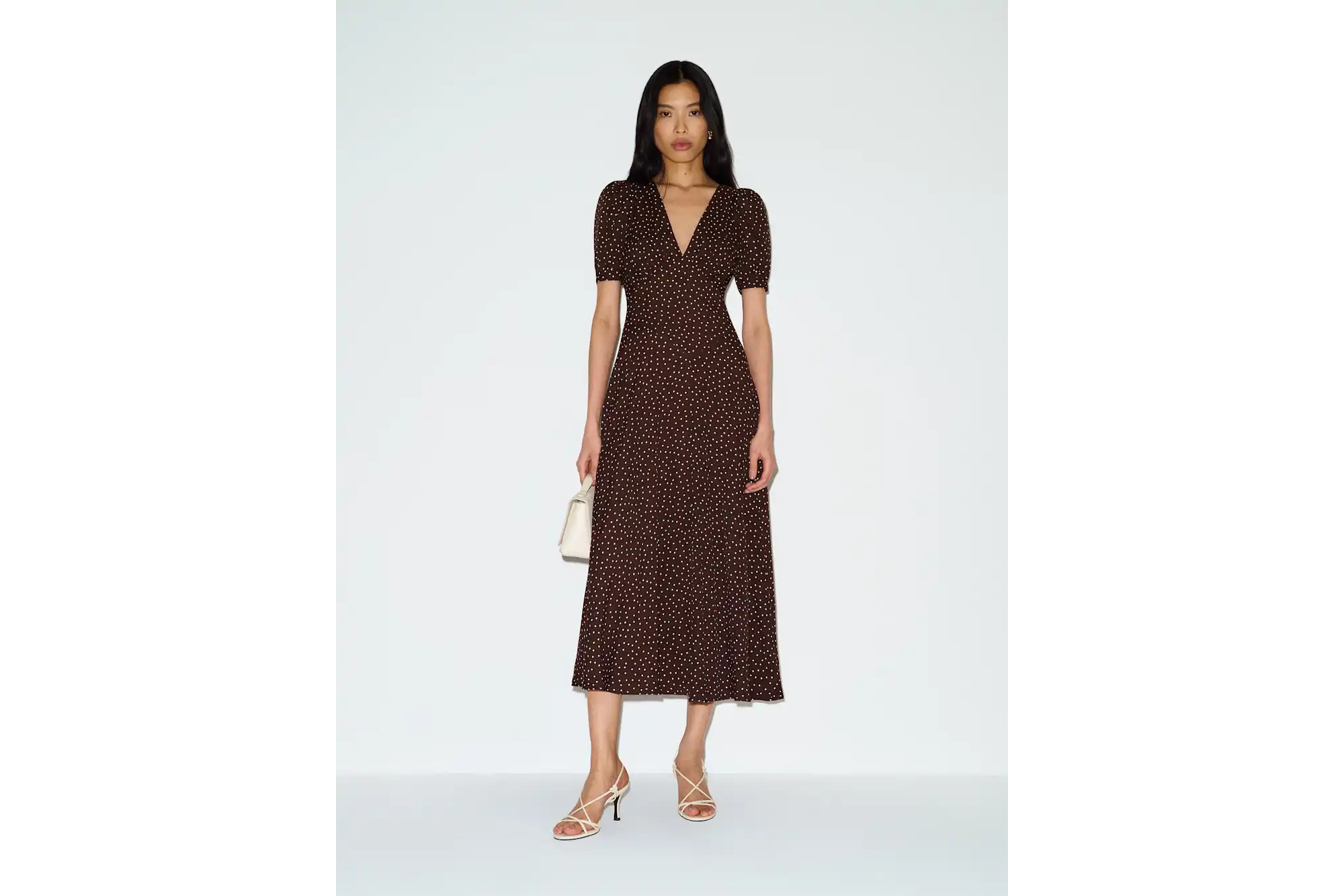 Woman in a brown polka-dot midi dress and white strappy heels.