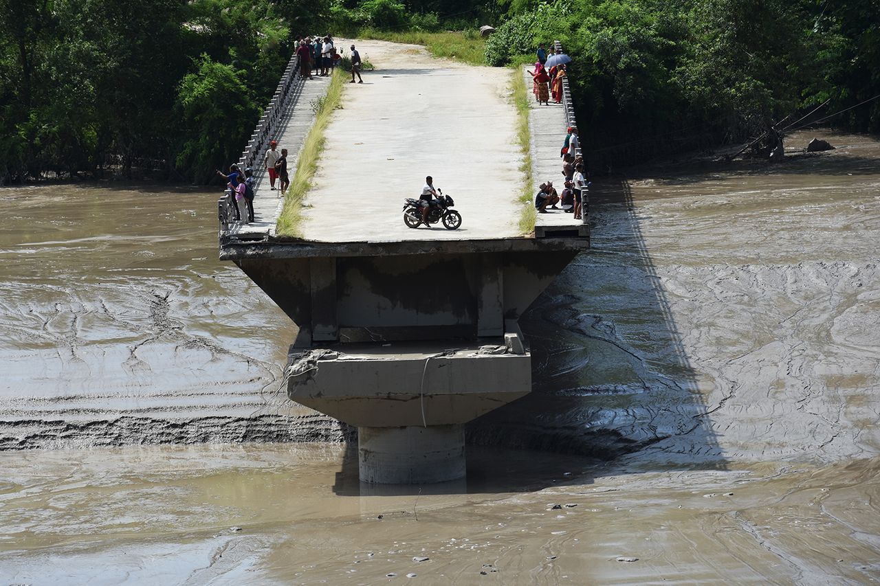 A resident rides a motorcycle on the remains of a bridge in Nepal’s Nuwakot district after flash flooding on Aug. 26, 2026Credit: Sunil Pradhan/Anadolu via Getty