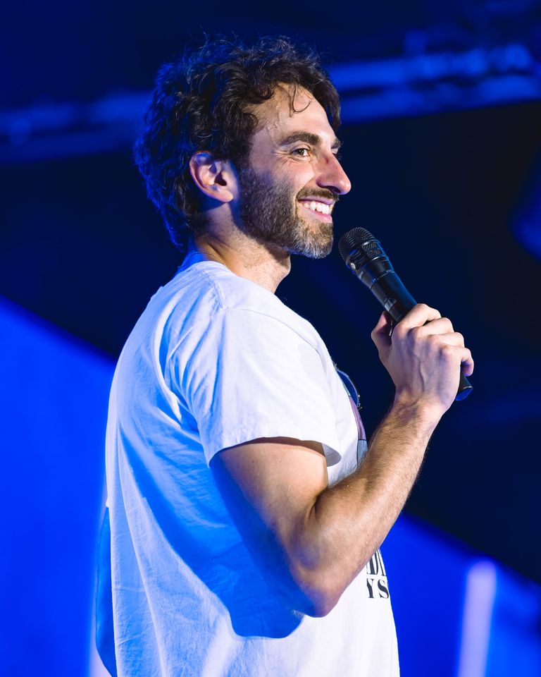 A man smiling while holding a microphone wearing a casual shirt facing a cheering audience Comedian Gianmarco Soresi brings the laughs to The Festival on Friday, Aug. 14 at Hutton Brickyards Riverfront Hotel + Venue in Kingston, N.Y.Credit: Austin Ruffer
