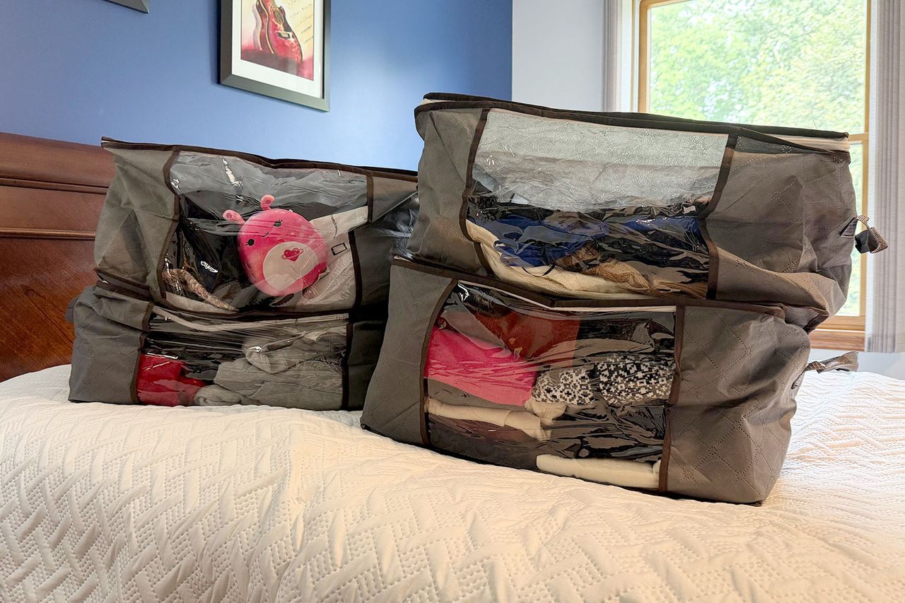 Fabric storage bags sitting on a bed filled with clothes and a stuffed toy visible through transparent panels Credit: People