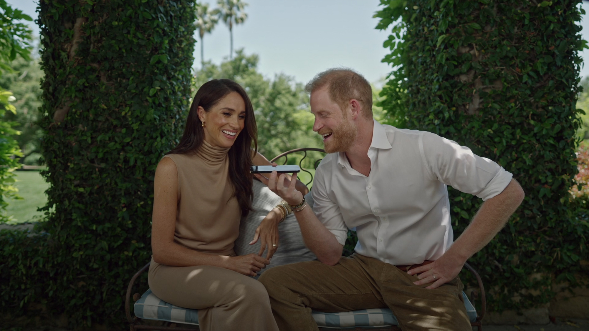 Meghan Markle and Prince Harry smiling and laughing while looking at a phone.
