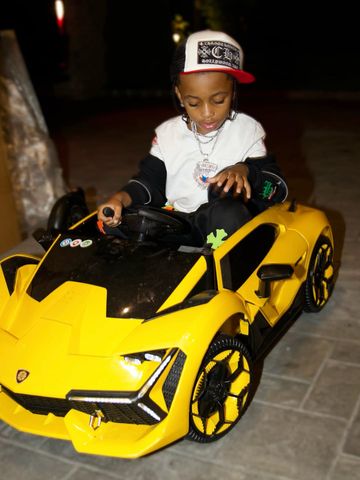 A child sitting in a toy car resembling a sports vehicle wearing a white sweatshirt and a baseball cap Wave drives a mini car at his birthday partyCredit: cardi b/instagram
