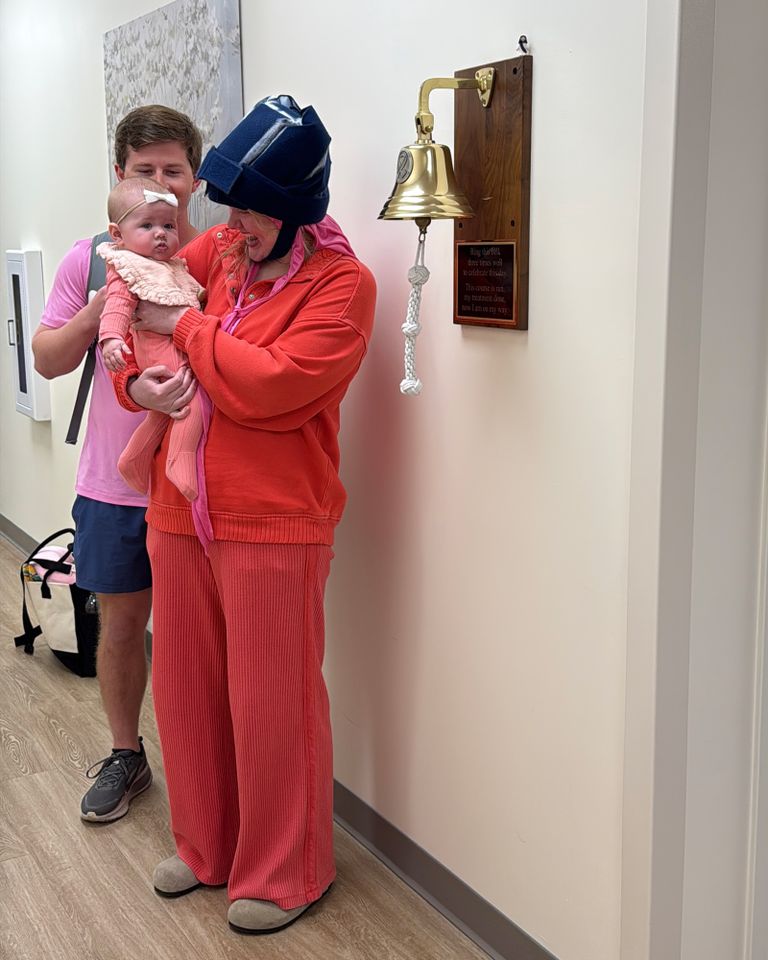 A person holding a baby near a bell mounted on a wall in a corridor another individual stands close behind holding items Abby Wilson and her familyCredit: Courtesy of Abby Wilson