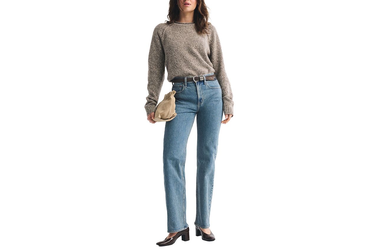 A person modeling highrise relaxed jeans and a sweater holding a clutch bag posed against a white background Credit: Abercrombie