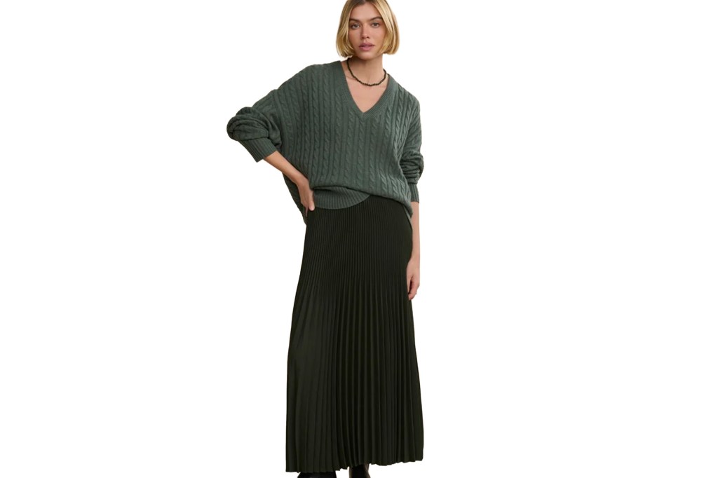 A woman in a green cable knit sweater and a dark green pleated maxi skirt.