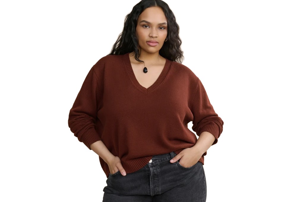 A woman wearing a brown V-neck sweater and dark jeans.
