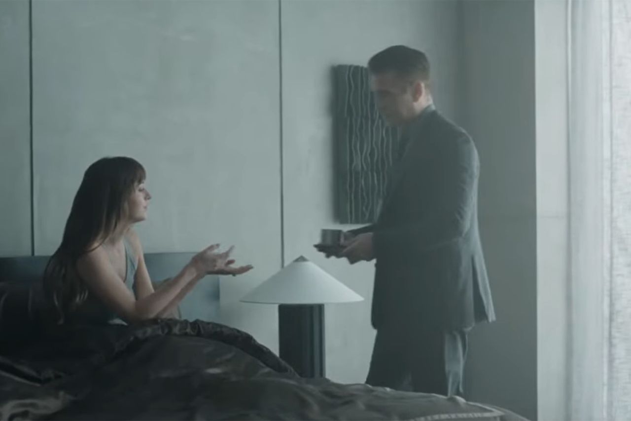 Two individuals in a modern room one sitting on a bed gesturing and the other standing holding an object Dakota Johnson and Colin Farrell in “Patient Zero”Credit: mtv